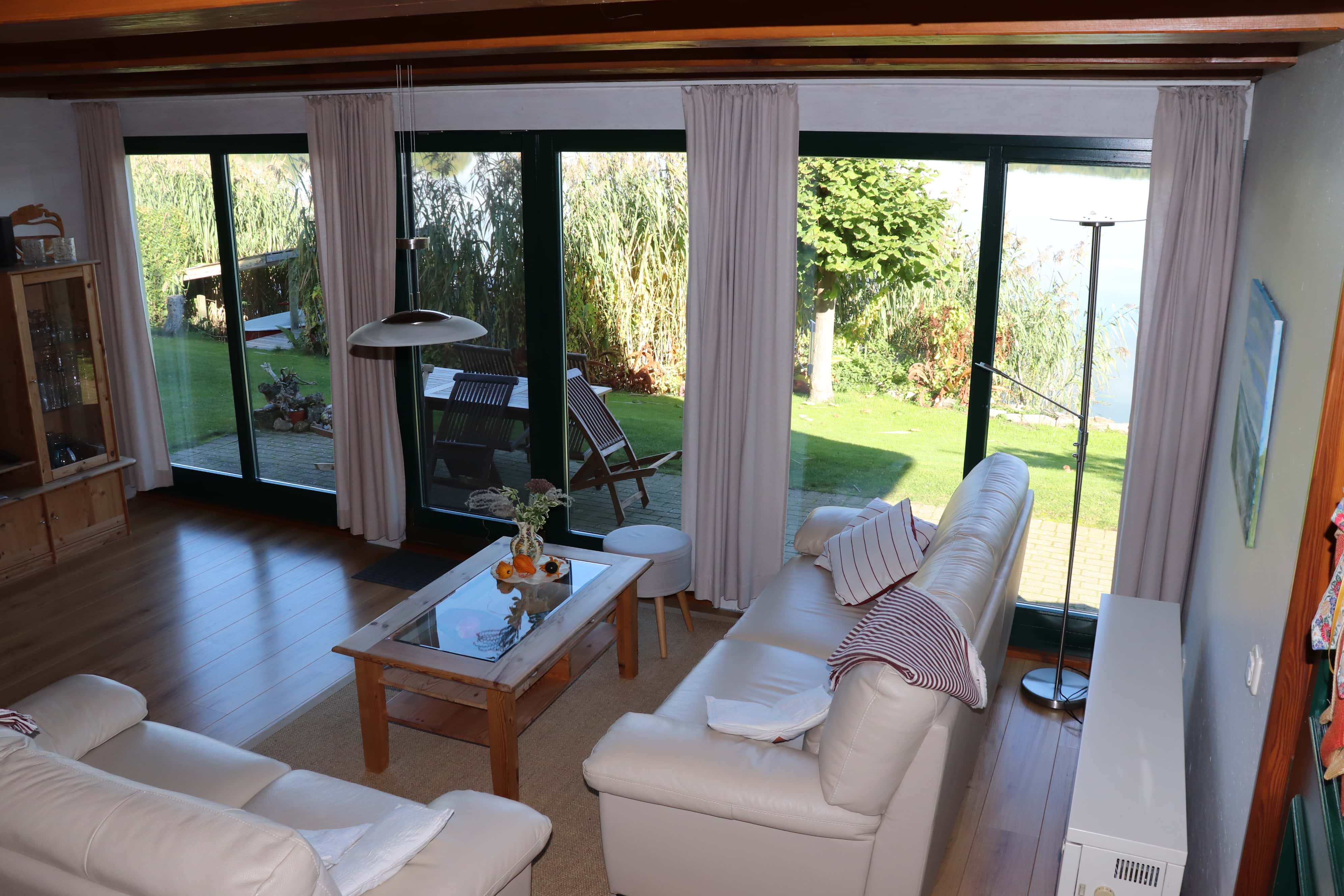 Innenansicht der Wohnstube mit zwei Couchgarnituren, einem Fernseher und Blick auf den Schilfgürtel vom Sternberger See.