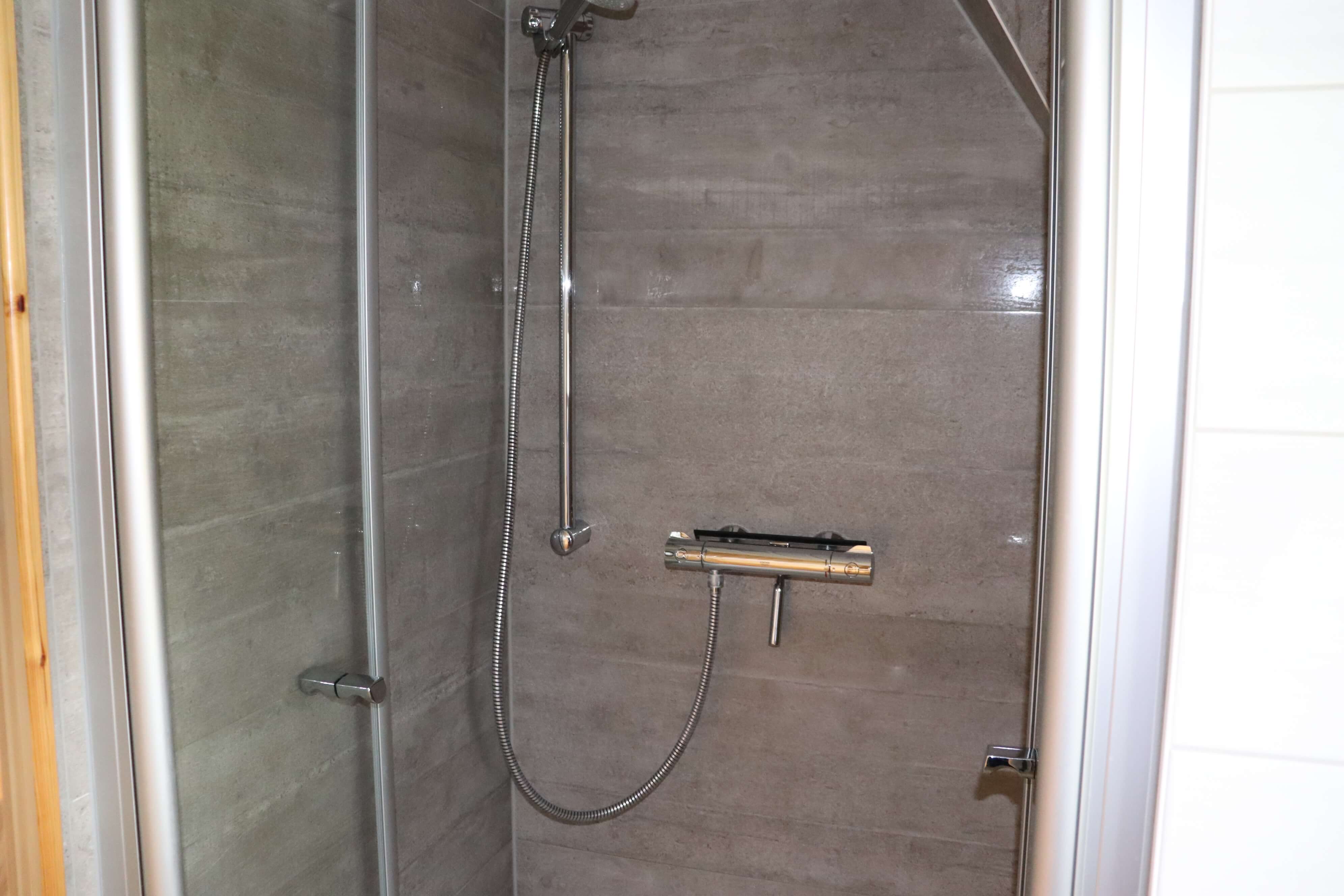 Bad mit weißen Fliesen und einer weißgestrichenen Holzdecke inklusive Toilette, Spiegel und Waschbecken.